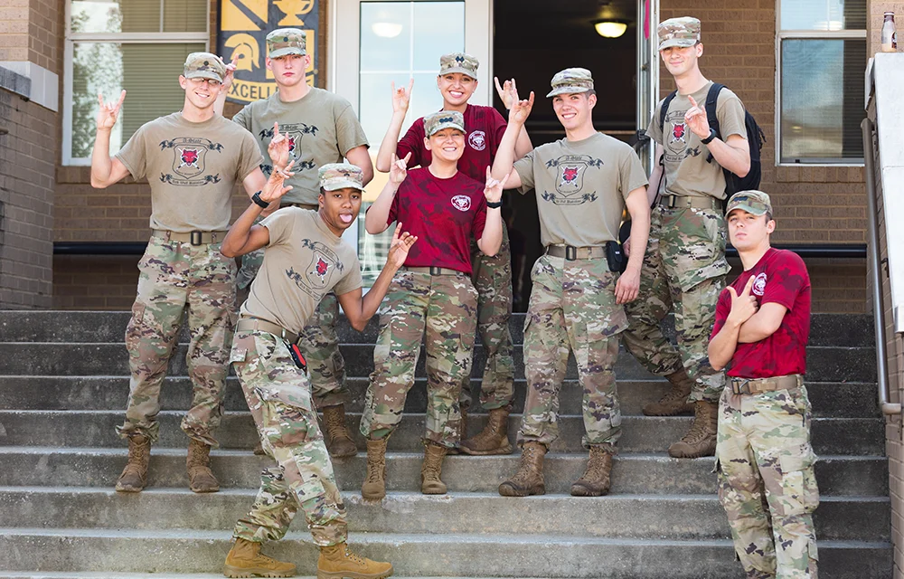 ROTC students standing on steps and giving Wolves Up.