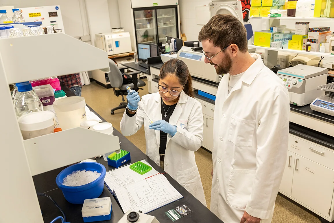 Two students in lab coats doing an experiment in a lab.