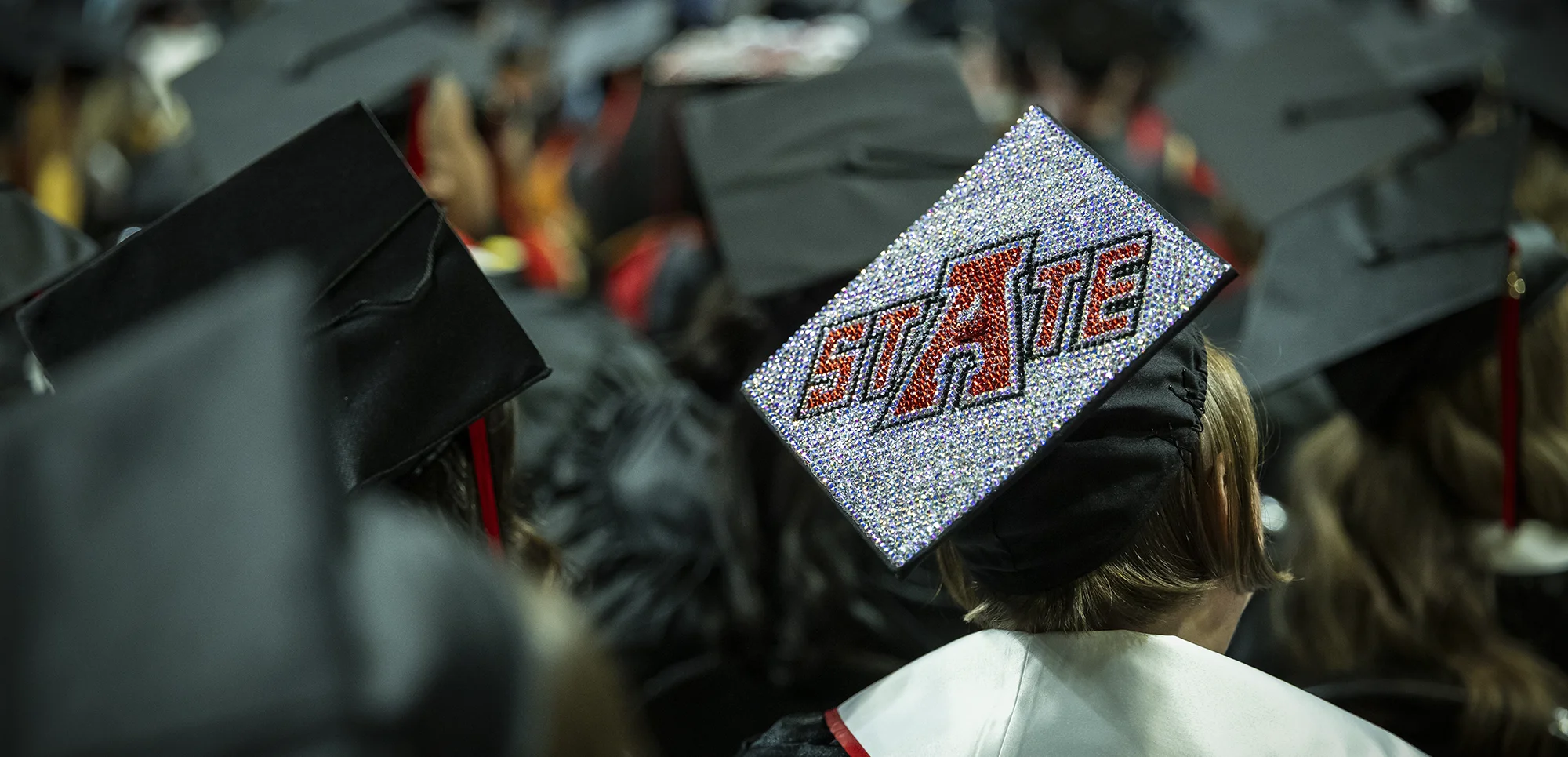 A sparkly graduation cap with the A-State logo in a sea of other graduation caps.