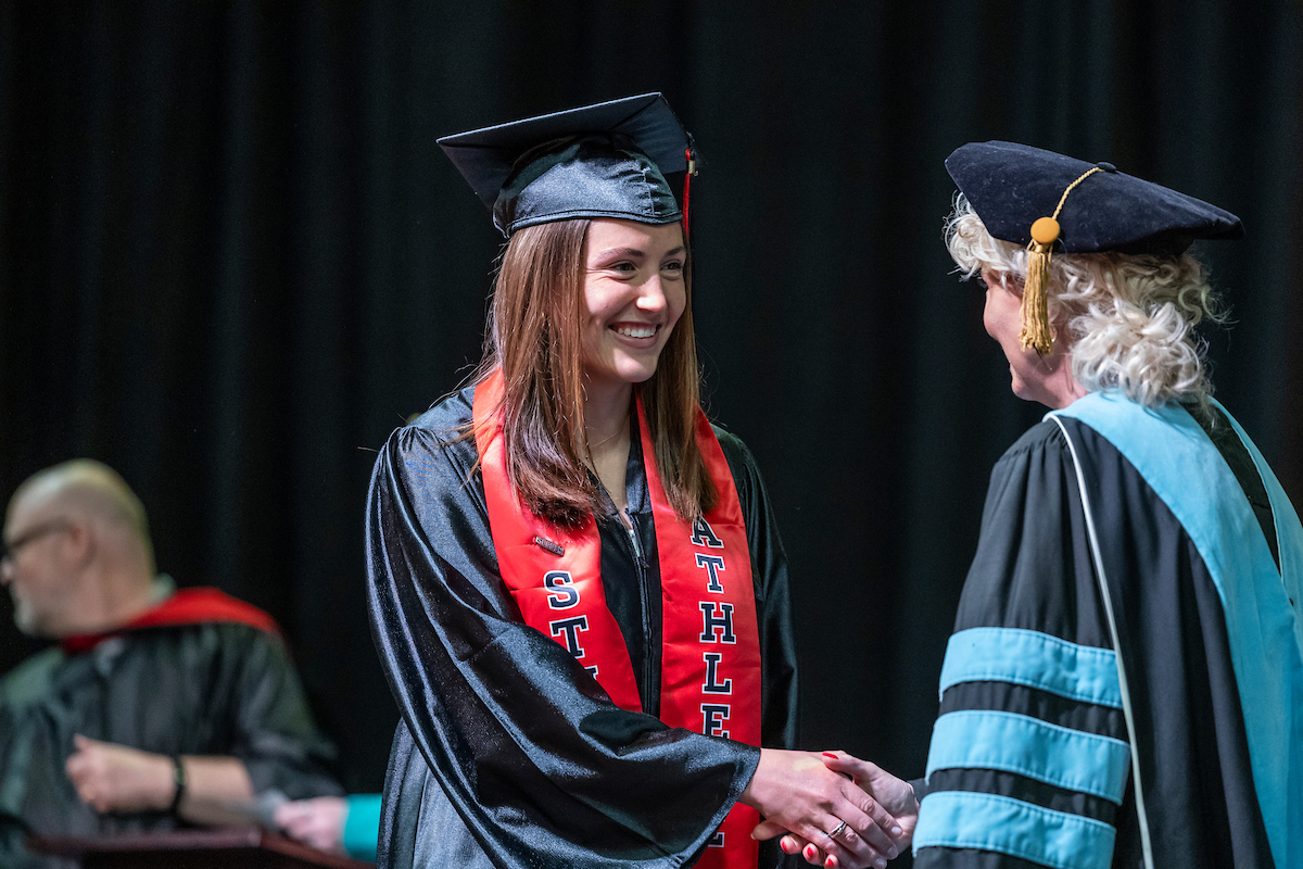 A-State student-athlete smiles while shaking hands at a graduation ceremony.