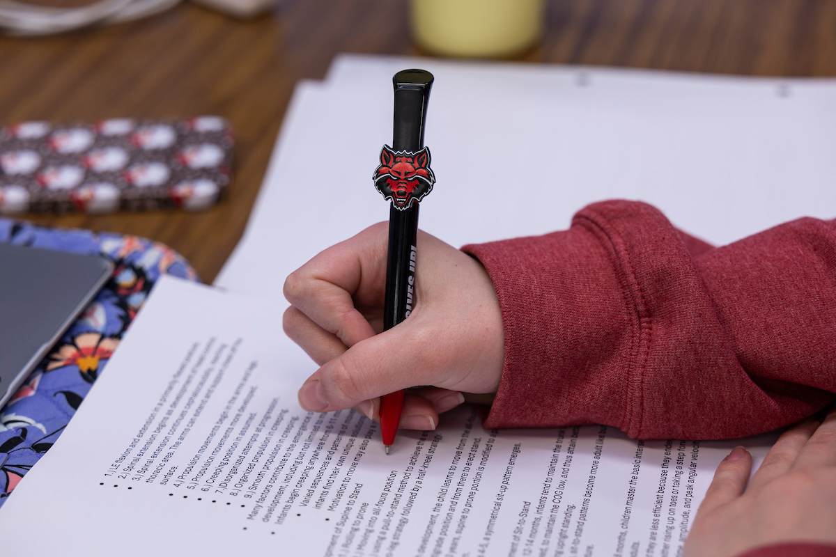 A student writes notes using a red wolf pen.
