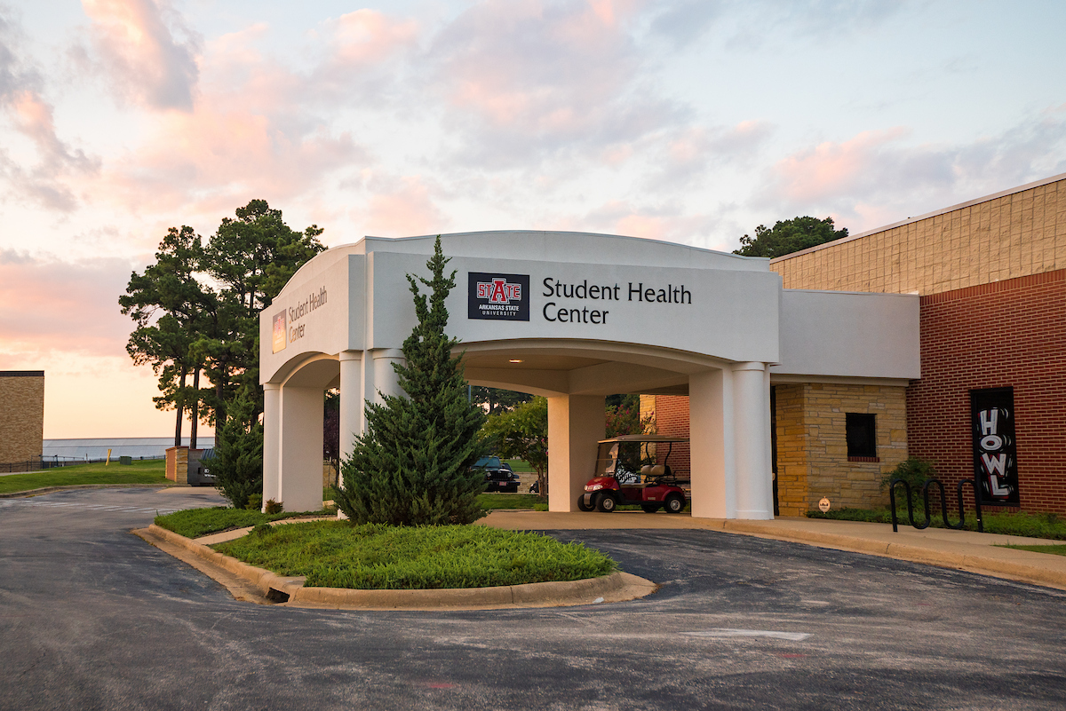 A-State Student Health Center entrance with A-State logo during sunset, surrounded by trees and brick walls.