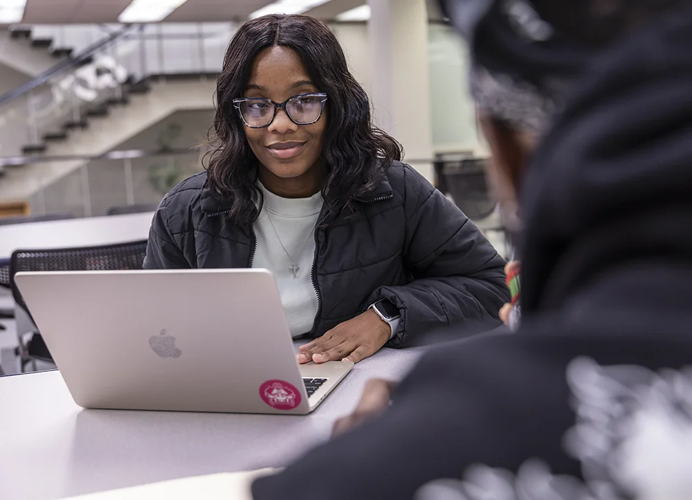 A student smiling at someone offscreen while using a laptop.