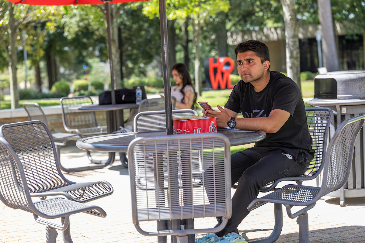 A Student has his phone out on a campus picnic table.
