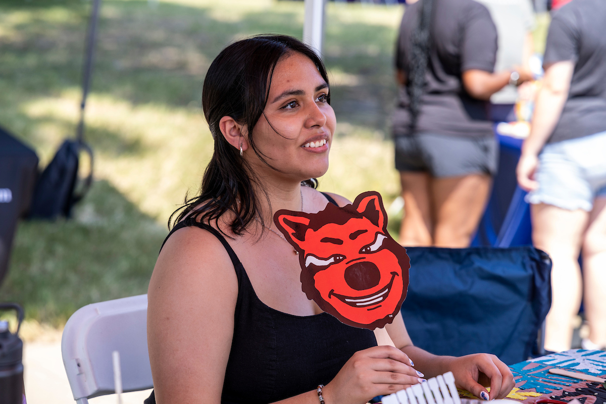  A student smiling and holding a sign with the A-State mascot Howl’s head on it.