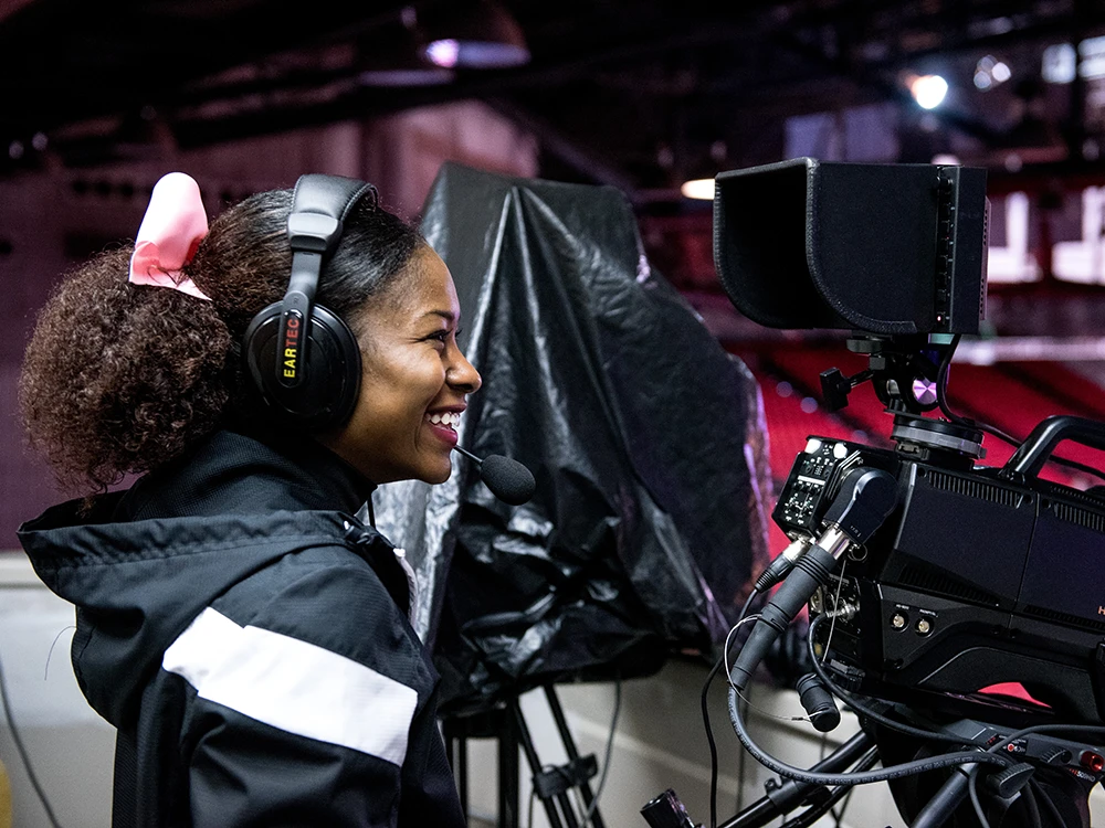 Student operating camera on basketball court.
