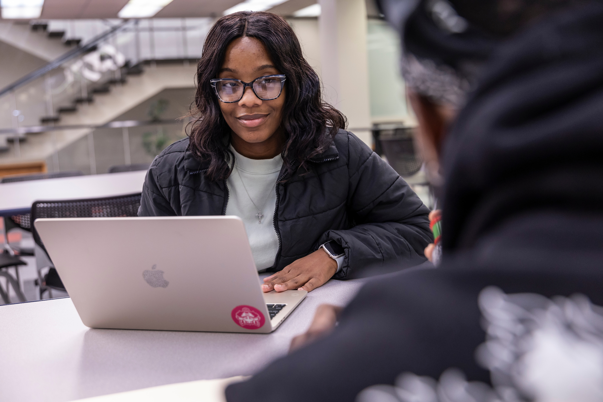 A student smiling at someone while working on laptops together in the library.