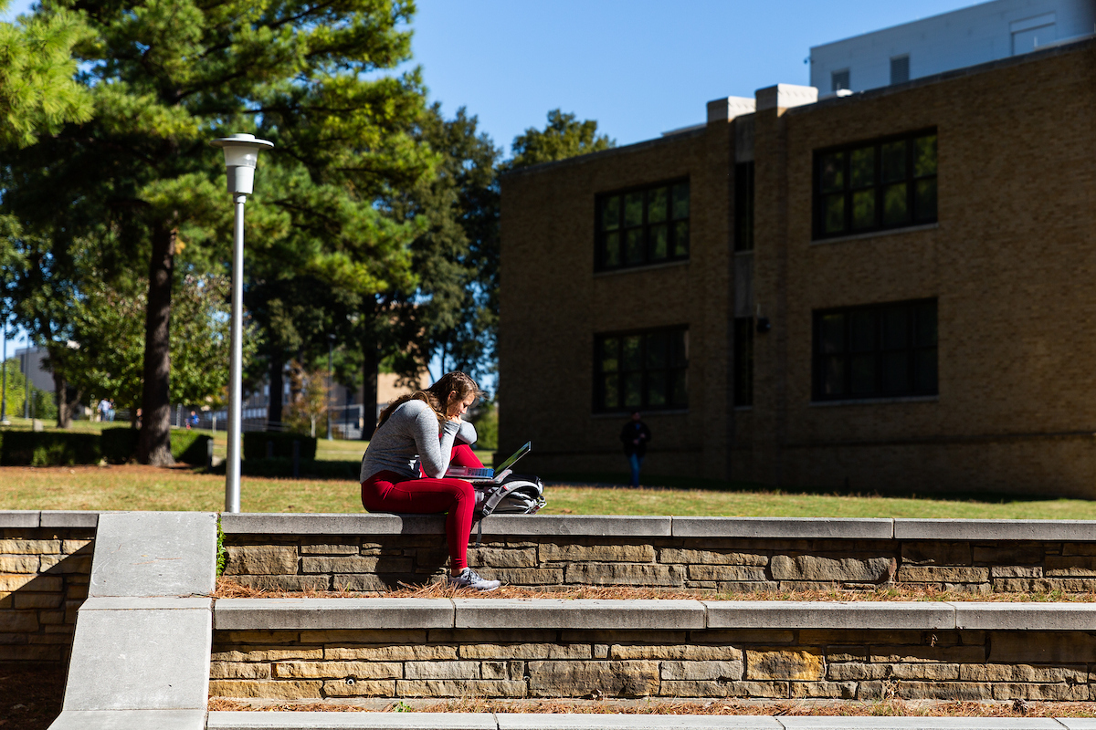 Student studies on outdoor campus steps with a laptop on a sunny fall day.