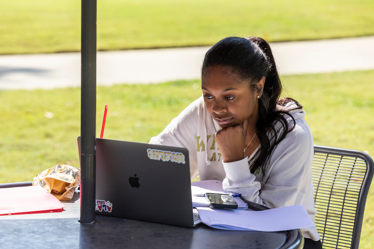 A student is in deep concentration while staring at a laptop screen at a picnic table.