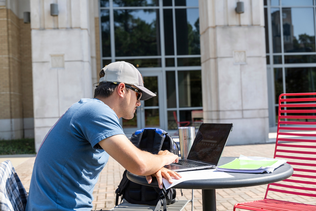 A student sitting outside the Humanities and Social Sciences building and using a laptop.