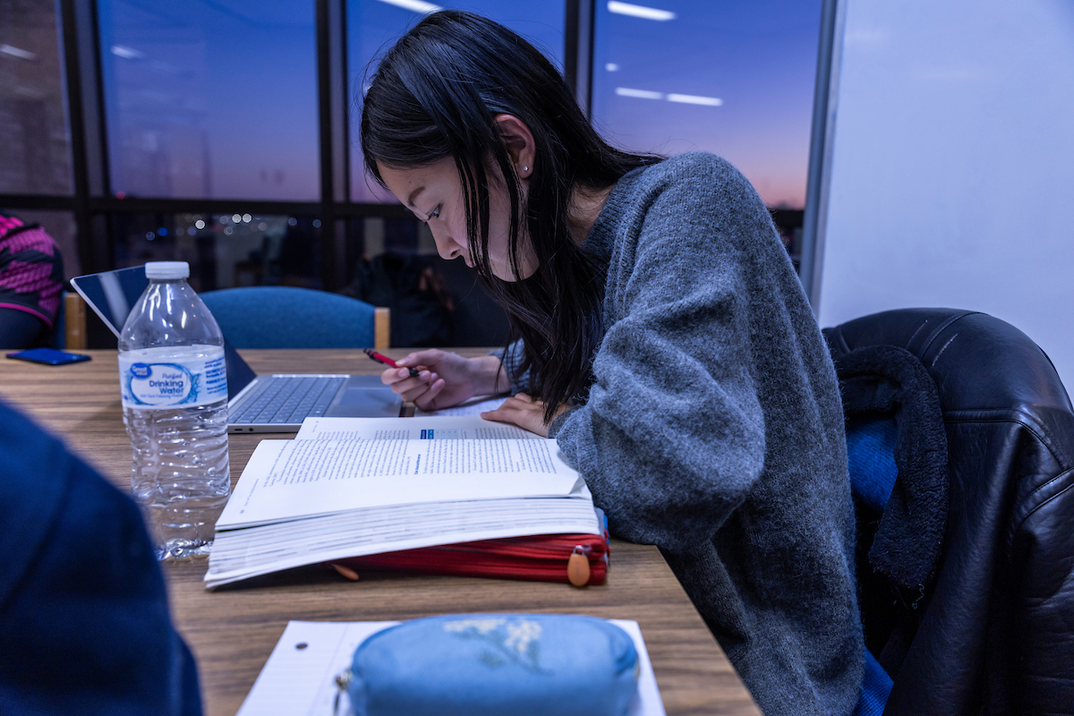 A-State student studies a textbook intently at a table during the evening with a laptop, water bottle, and notebook nearby.