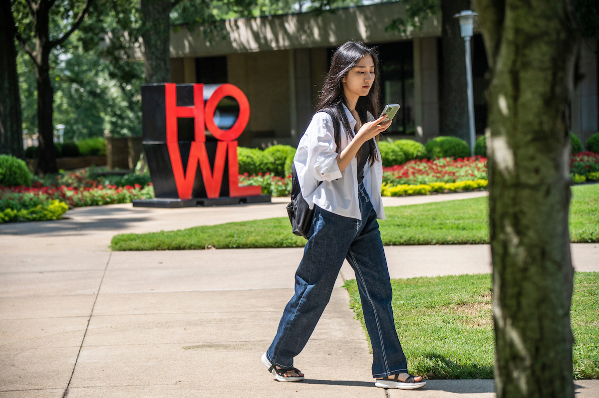 Student walks across campus on a sunny day.