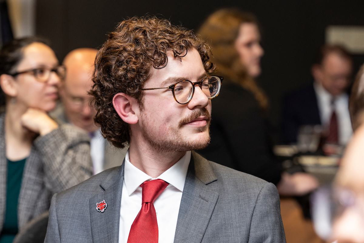 Student in suit and red tie with Red Wolves pin attends an awards ceremony.
