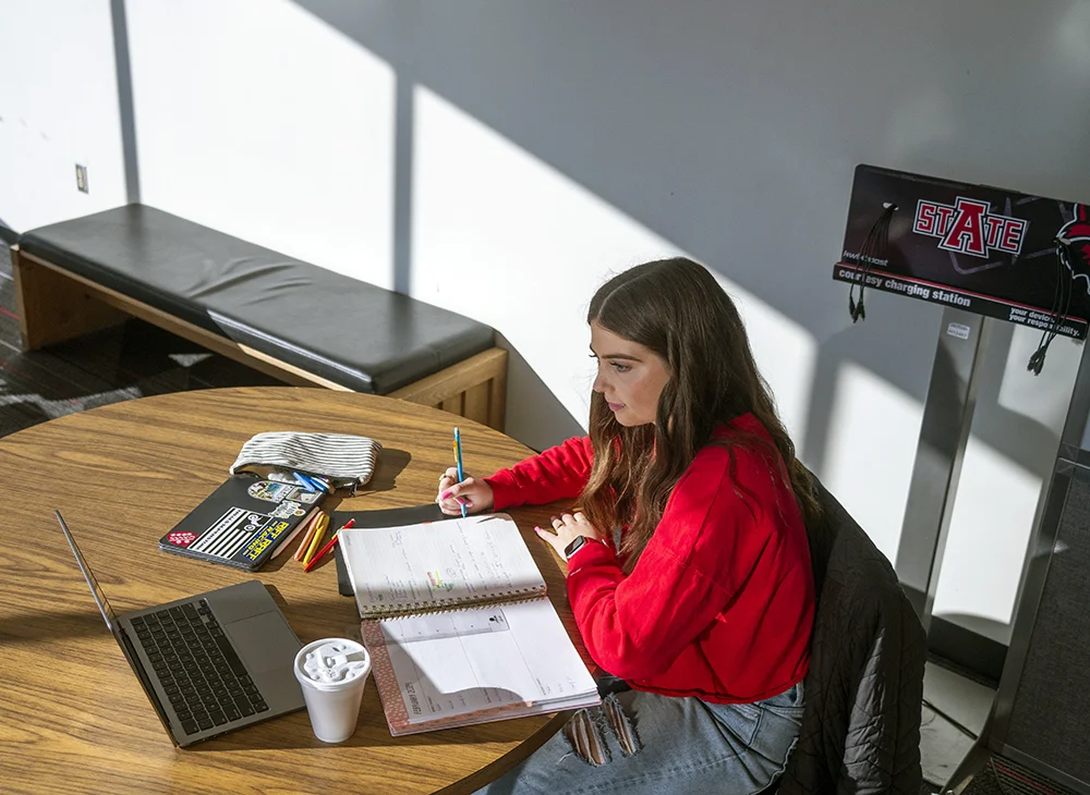 Student with laptop writing in a notebook
