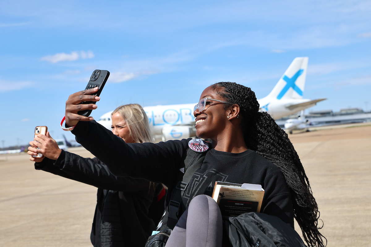 A-State students taking selfies on the runway with an airplane in the background before the flight.