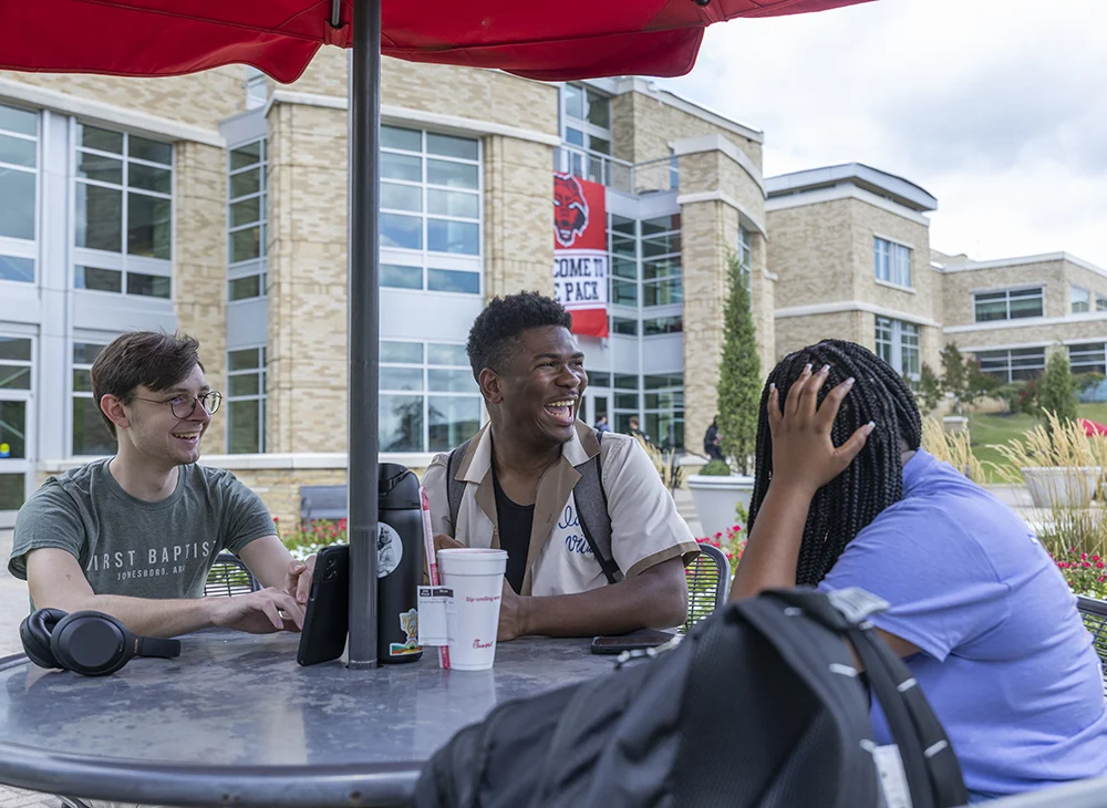 Three students laughing at table together.