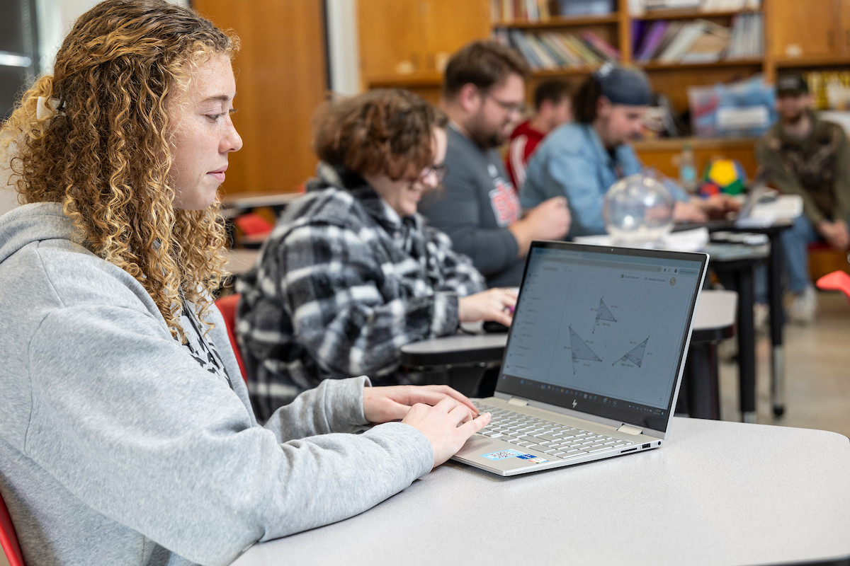 A student checks a laptop while sitting at a table in class.