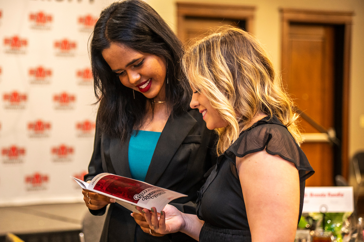 Two A-State students read an event program together at an indoor Red Wolves gathering.