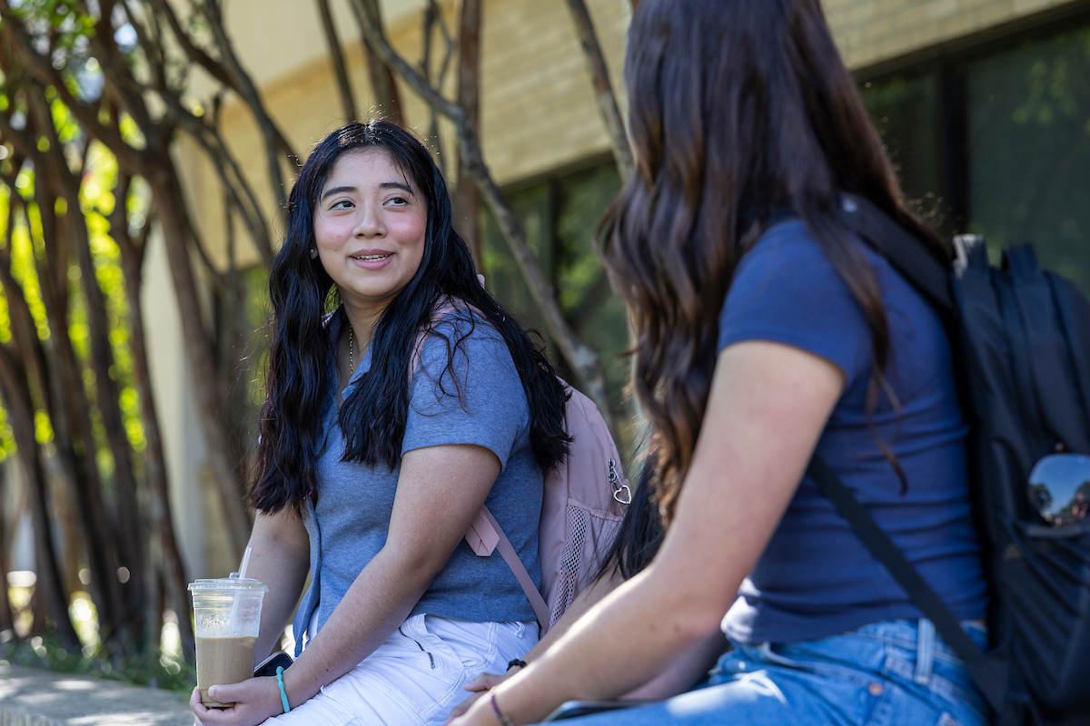 Two students talking while sitting outside.