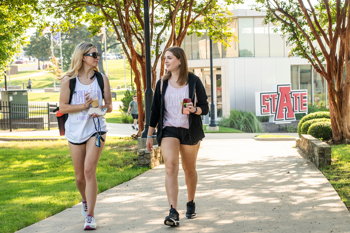 Two students walking on campus near the Welcome Center on a sunny day.