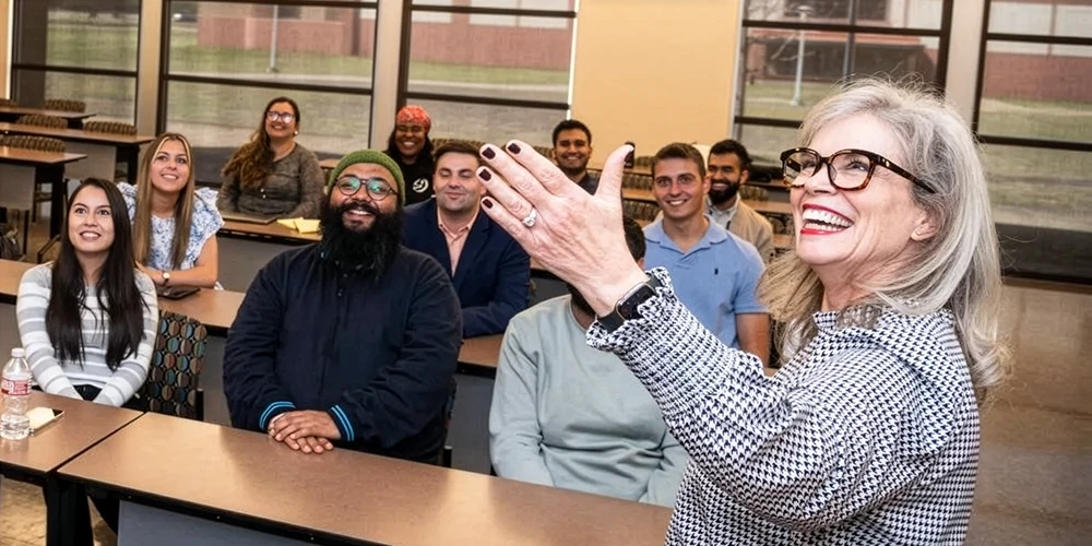 Communications teacher gesturing and smiling in front of class.