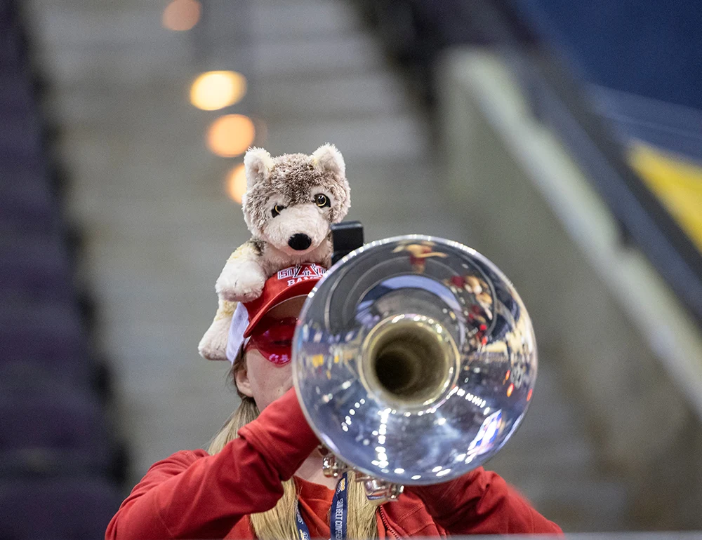 Student playing trumpet with a wolf plush on their head.