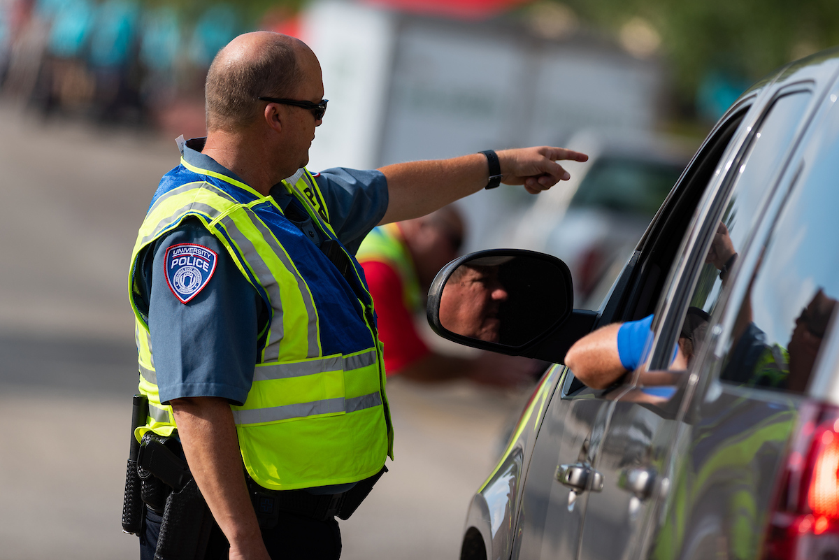 University police officer in reflective vest points while talking to a driver during campus move-in day.