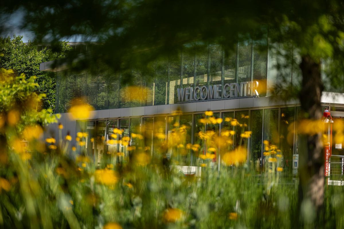  Yellow flowers bloom in front of AState’s glass-paneled Welcome Center on a bright spring day.