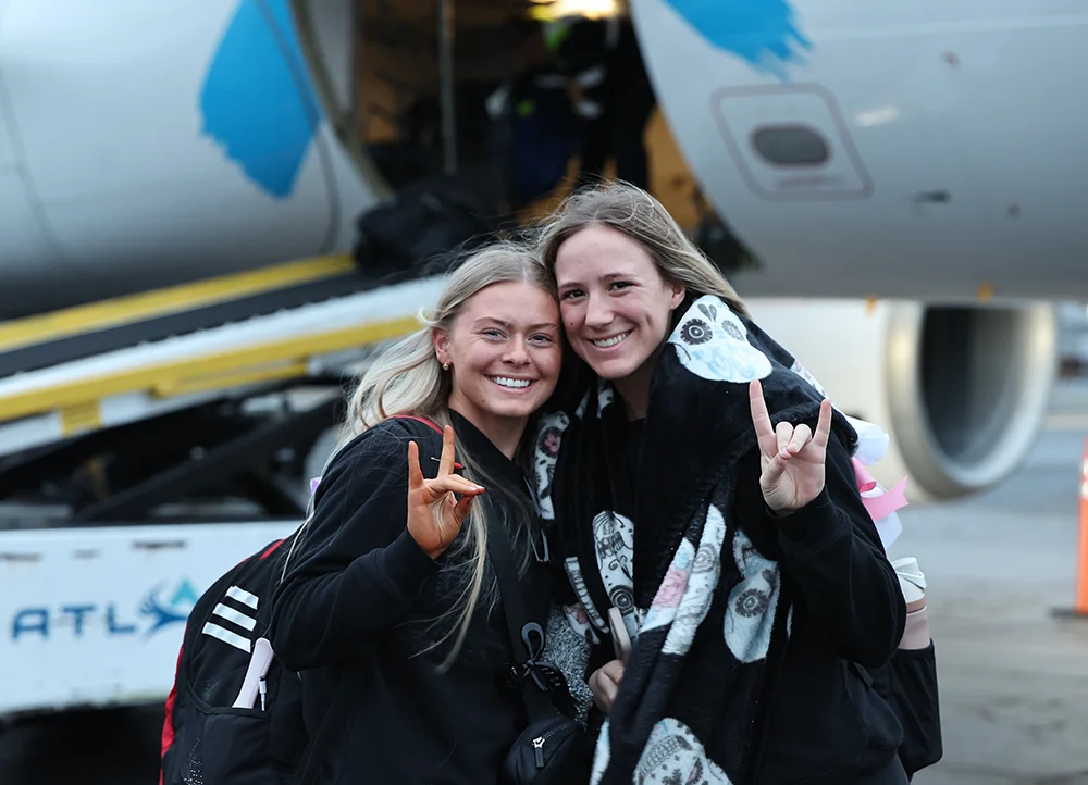 Two students giving Wolves Up before getting on an airplane.