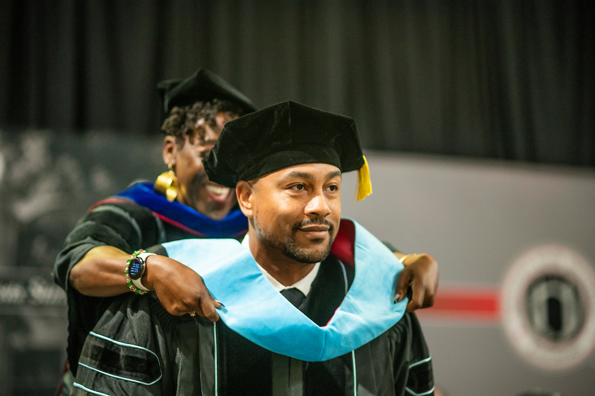 Graduate receives academic hood during A-State commencement ceremony in formal regalia.