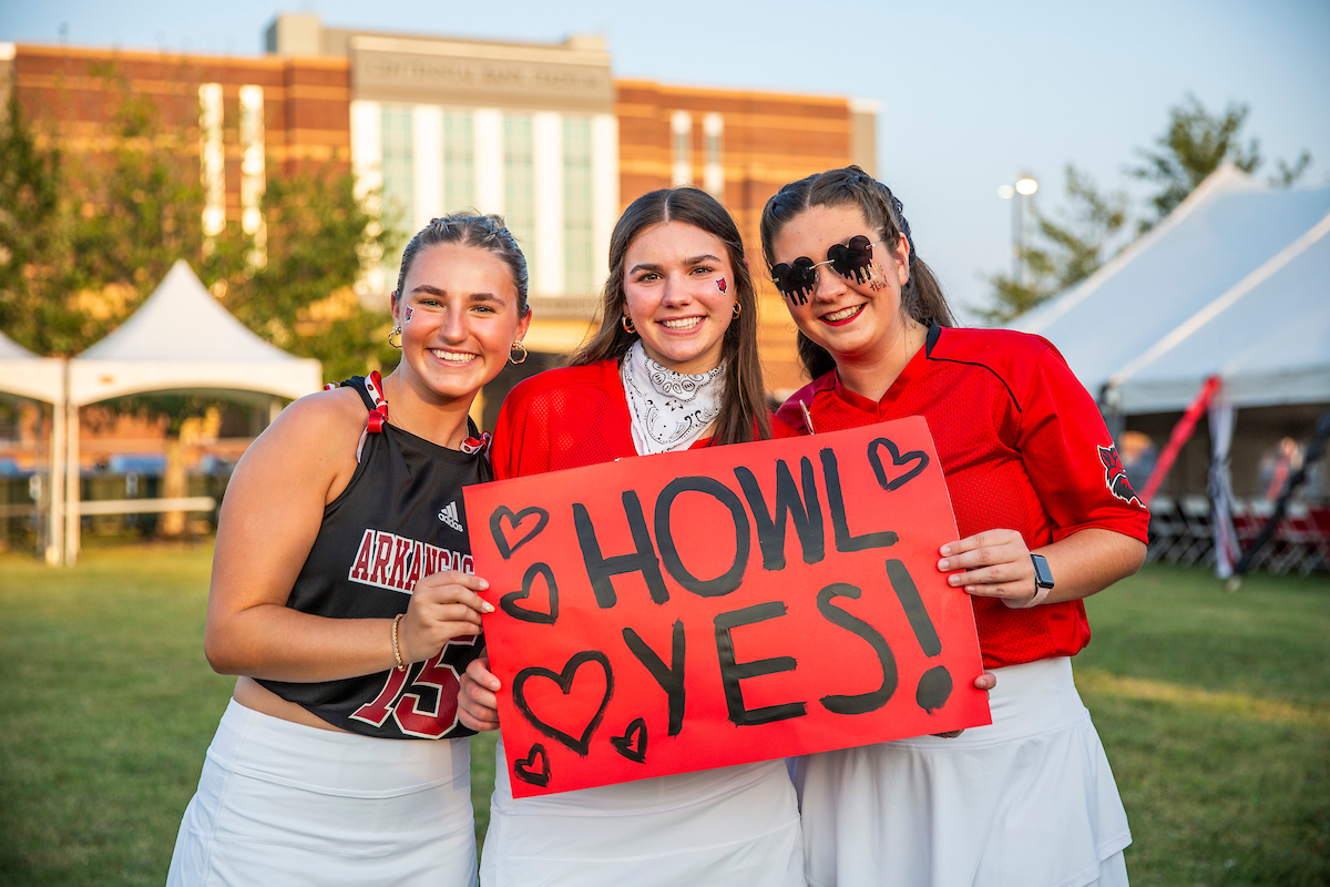 Students hold a HOWL YES sign in front of Centennial Bank Stadium.