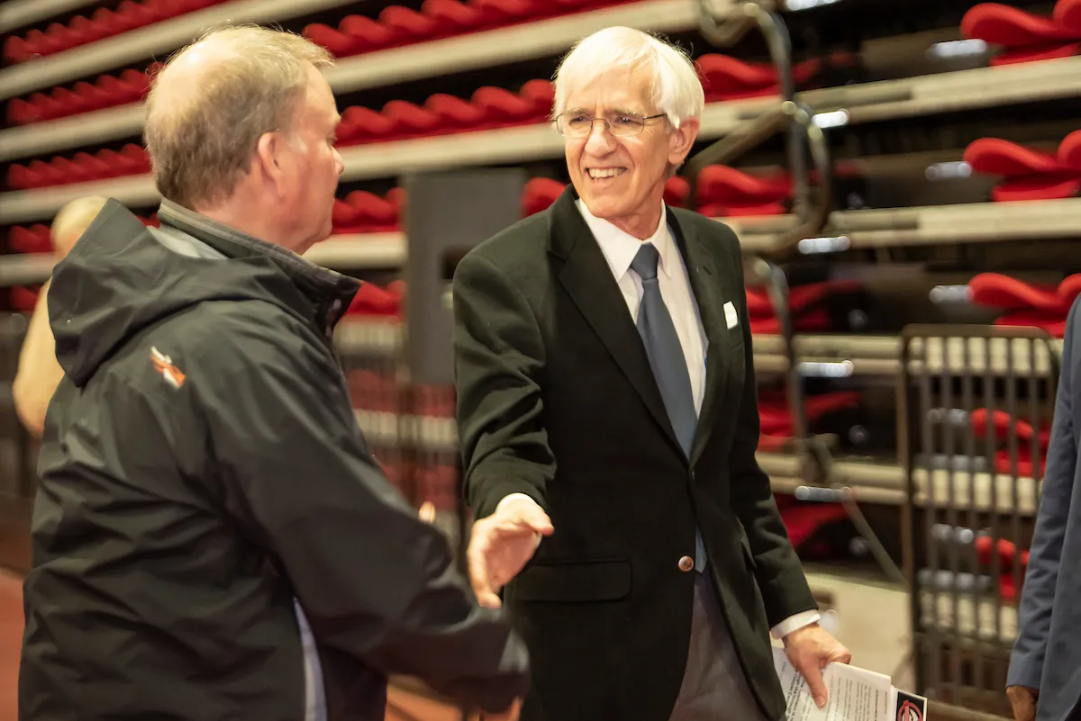 A faculty member in a suit smiles and shakes hands during a university event.