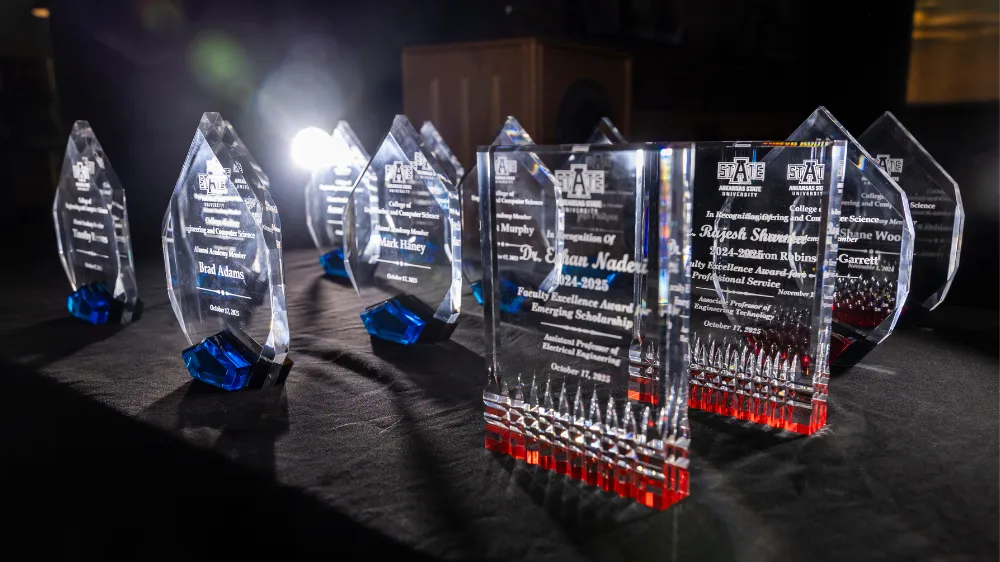 Alumni Academy glass awards setting on a black table with a light in the background.
