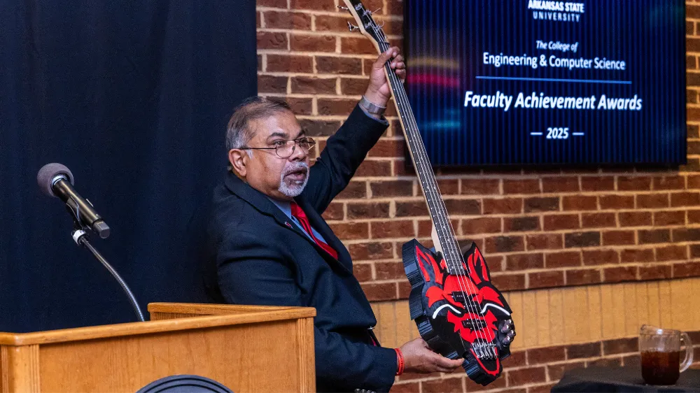 Dr. Bhattacharya holding a redwolf logo shaped bass guitar during the awards.