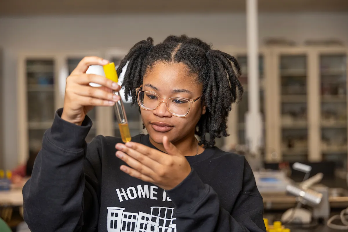 Student carefully observes yellow liquid in pipette during chemistry lab.