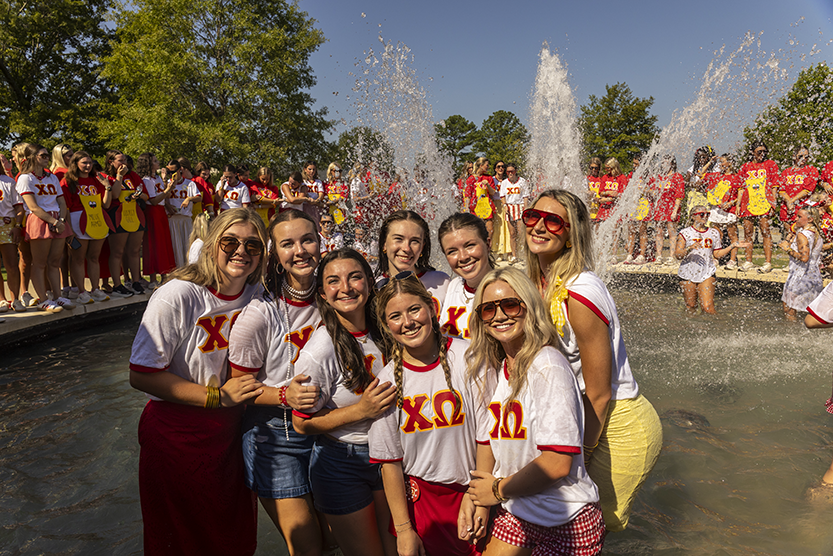 Group of individuals wearing matching shirts pose in Chi Omega fountain on campus.