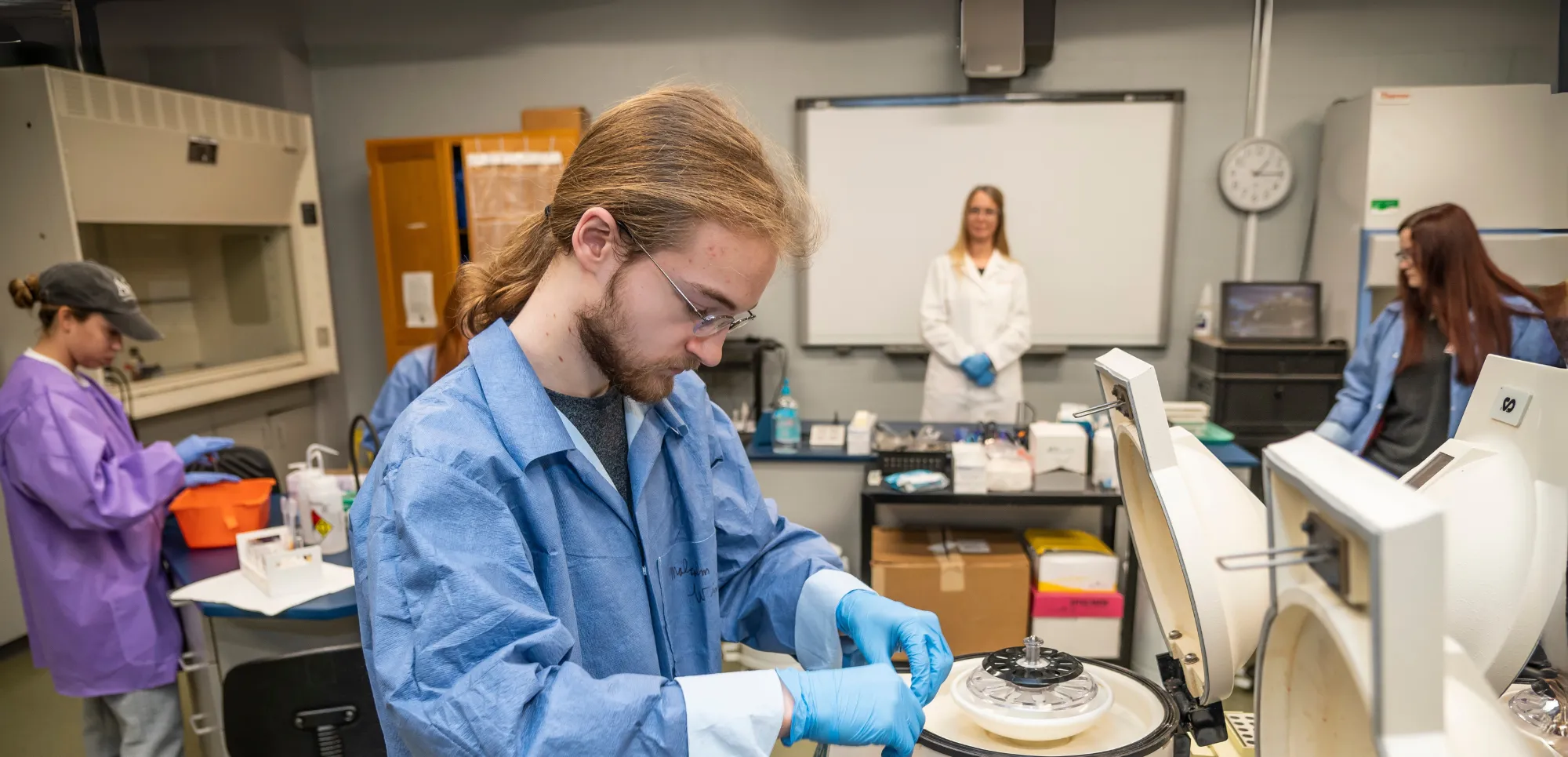 Clinical Lab students using microscopes in lab with teacher.
