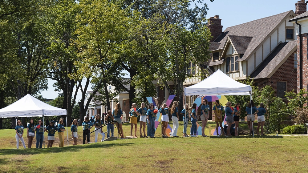 Group gathered inside a doorway wearing matching shirts, clapping and welcoming guests during recruitment.
