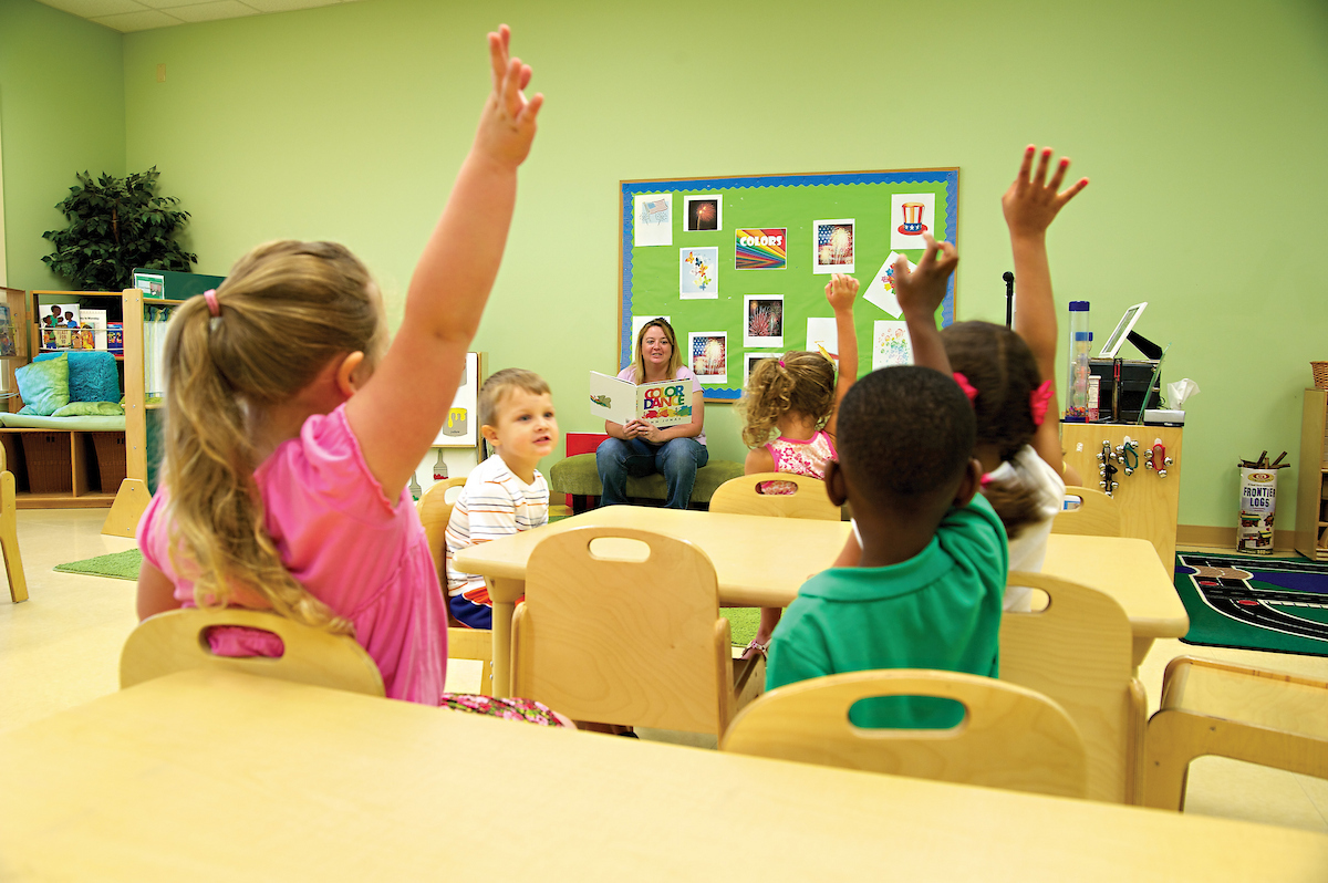 Young children raise their hands in an early childhood classroom at Arkansas State.