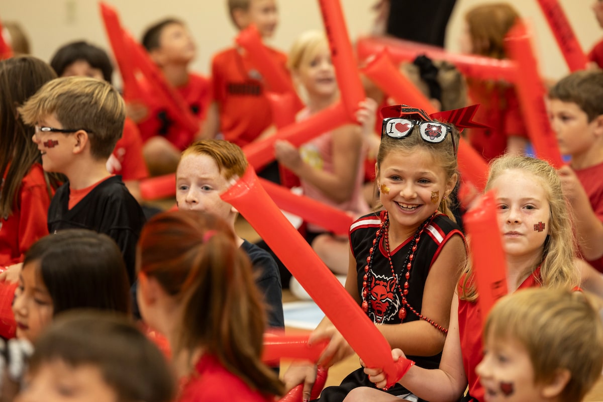 Children in Red Wolves gear cheer with inflatable noisemakers.