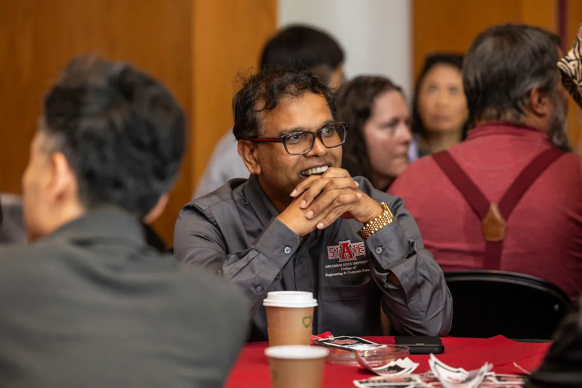 A faculty member smiles while seated at a table during a university gathering.