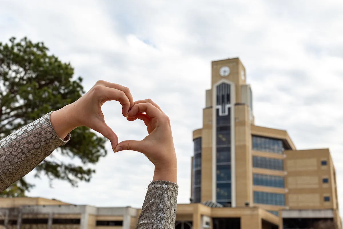 A student makes heart hands in front of the Dean B. Ellis Library