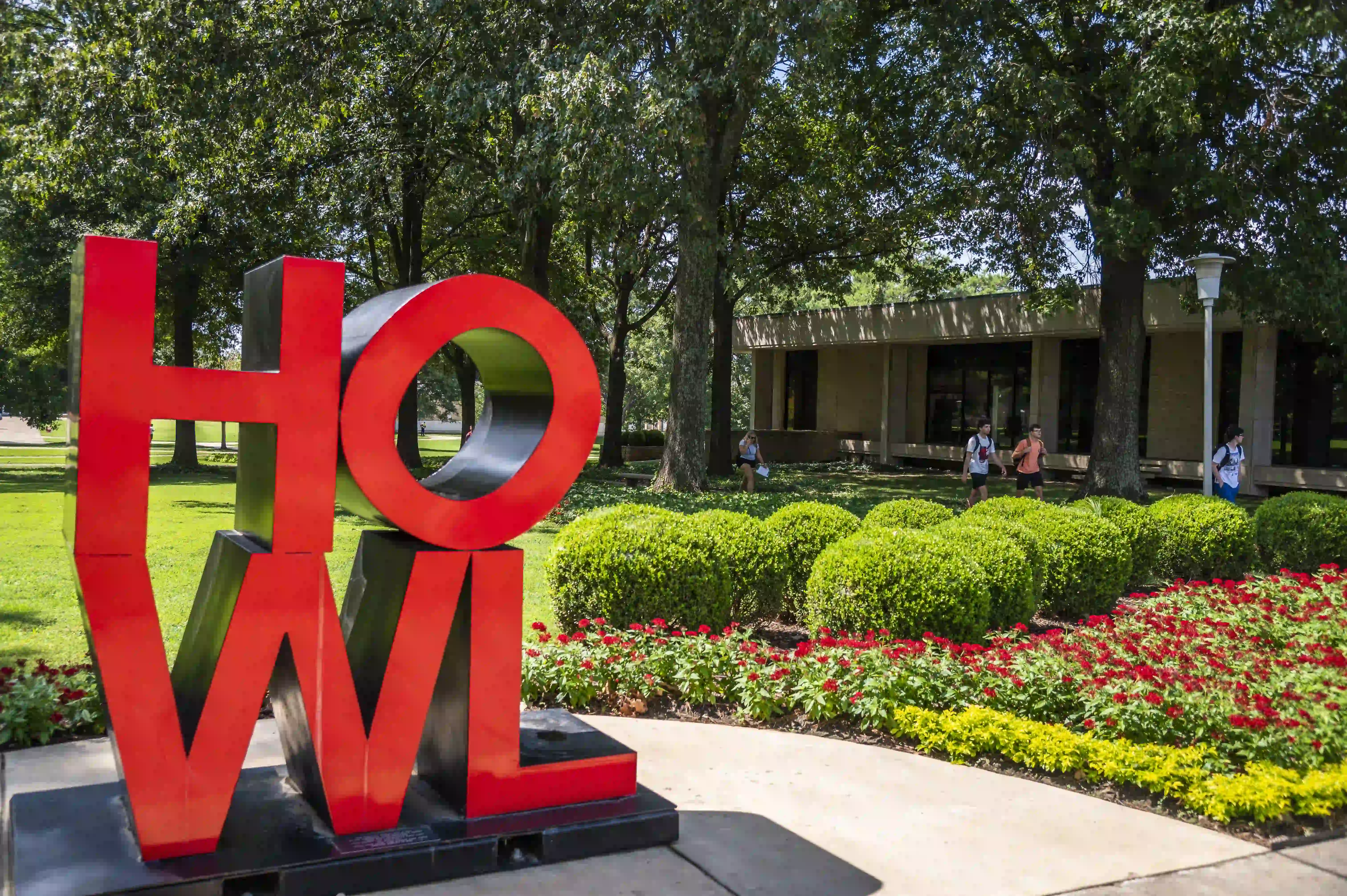 HOWL statue in front of green shrubs and blooming flowers outside the Administration building at Arkansas State University.