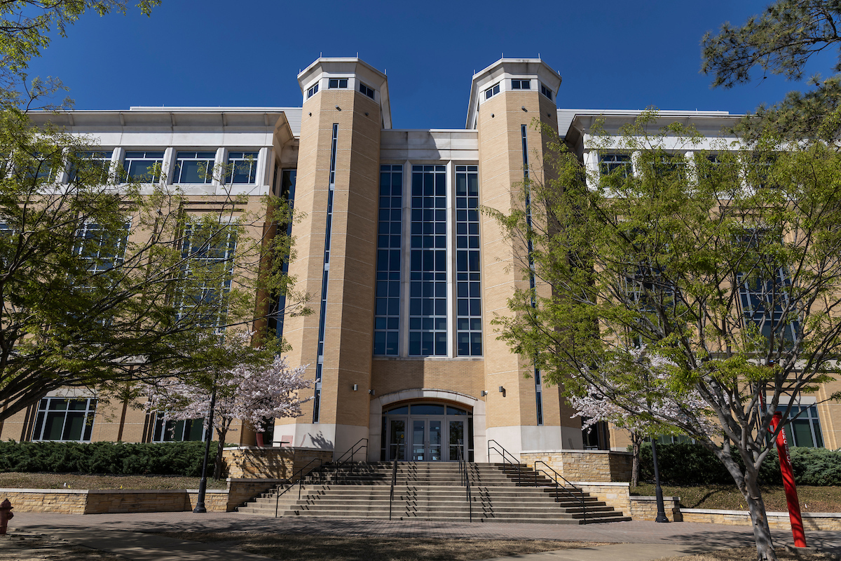 Exterior view of A-State building entrance with spring trees and blue sky.