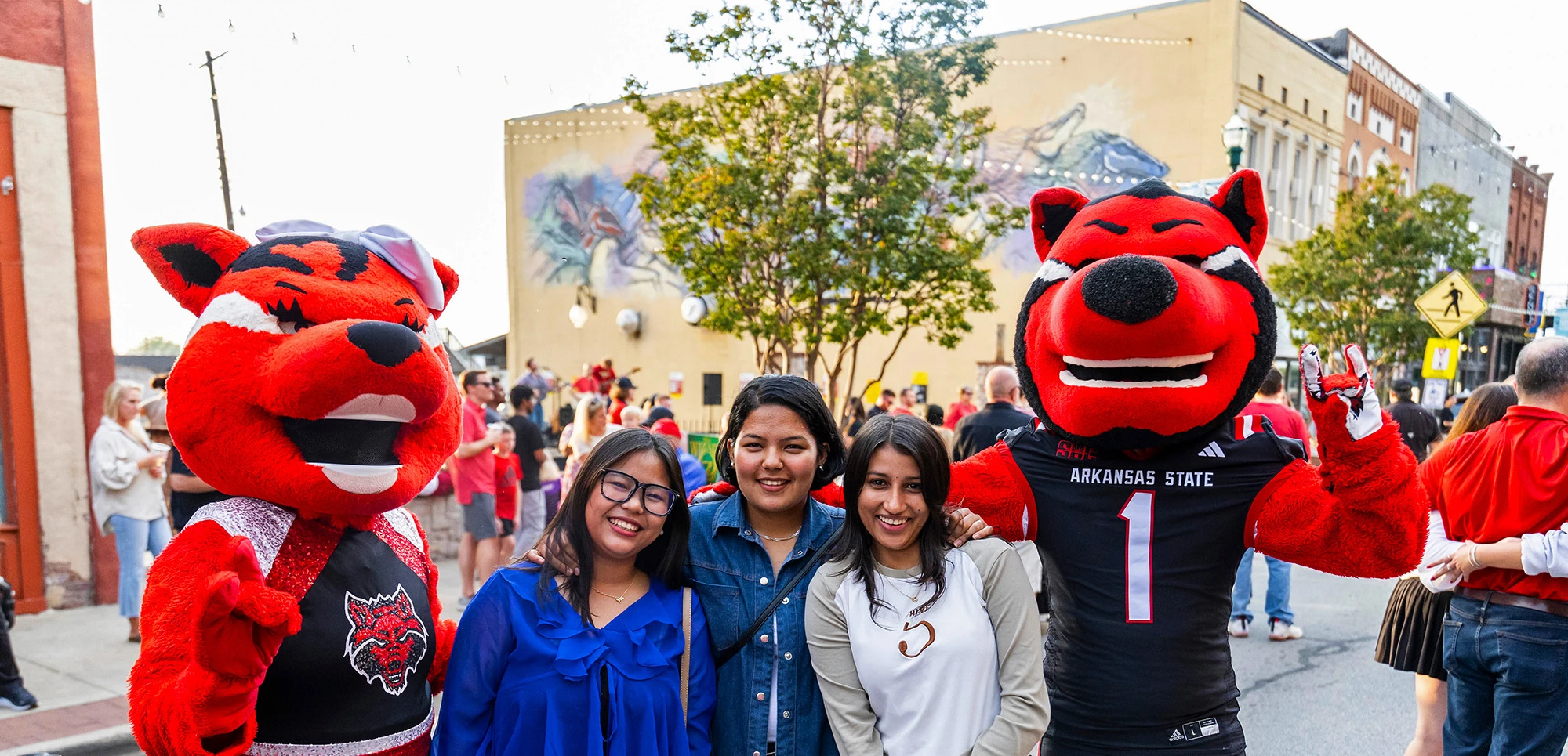 Howl and Scarlet with three smiling students at a downtown Jonesboro festival