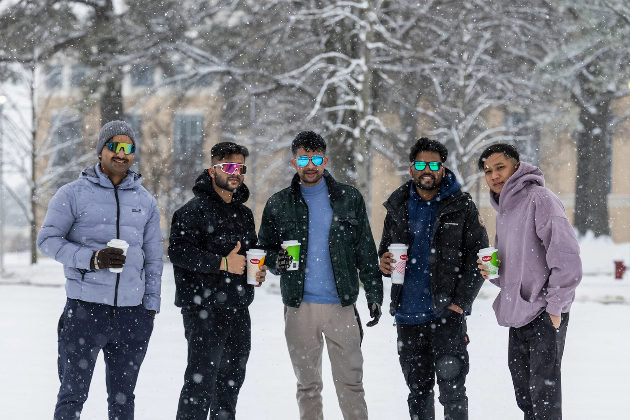 5 international students posing in the snow while holding cups of coffee