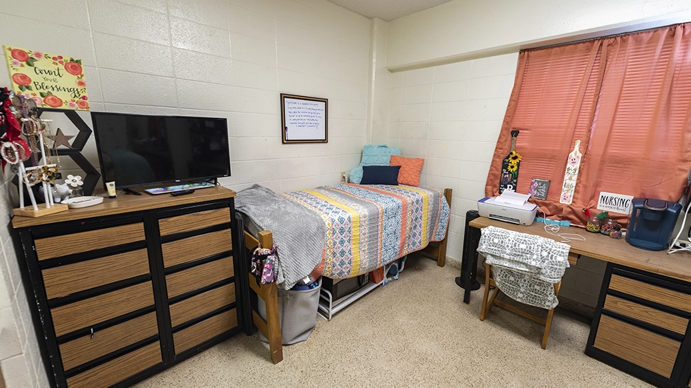 Bedroom with colorful bedding, dresser, and desk in Kays Hall suite.