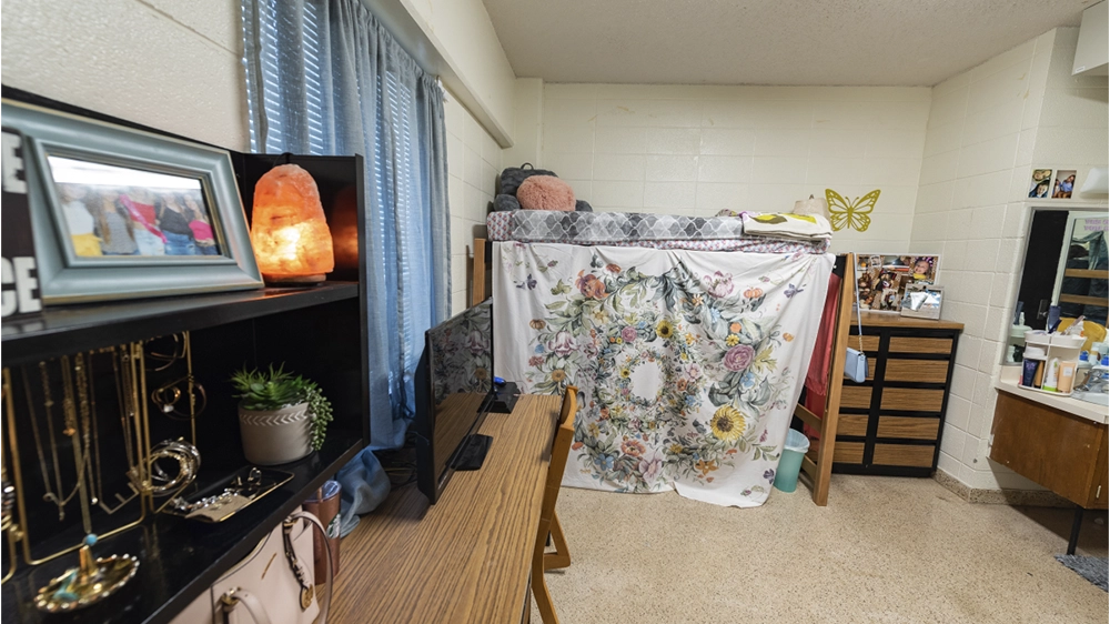 Lofted bed with floral curtain, long desk with shelving, and dresser in Kays Hall room.