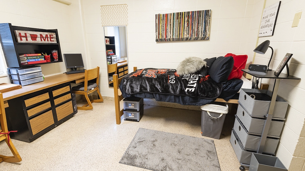 Single bed with black bedding, long desk with drawers, and storage organizer in Kays Hall room.