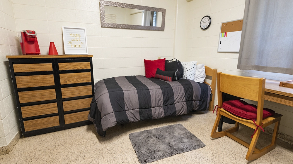 Single bed with black bedding, dresser, and desk in Kays Hall room.